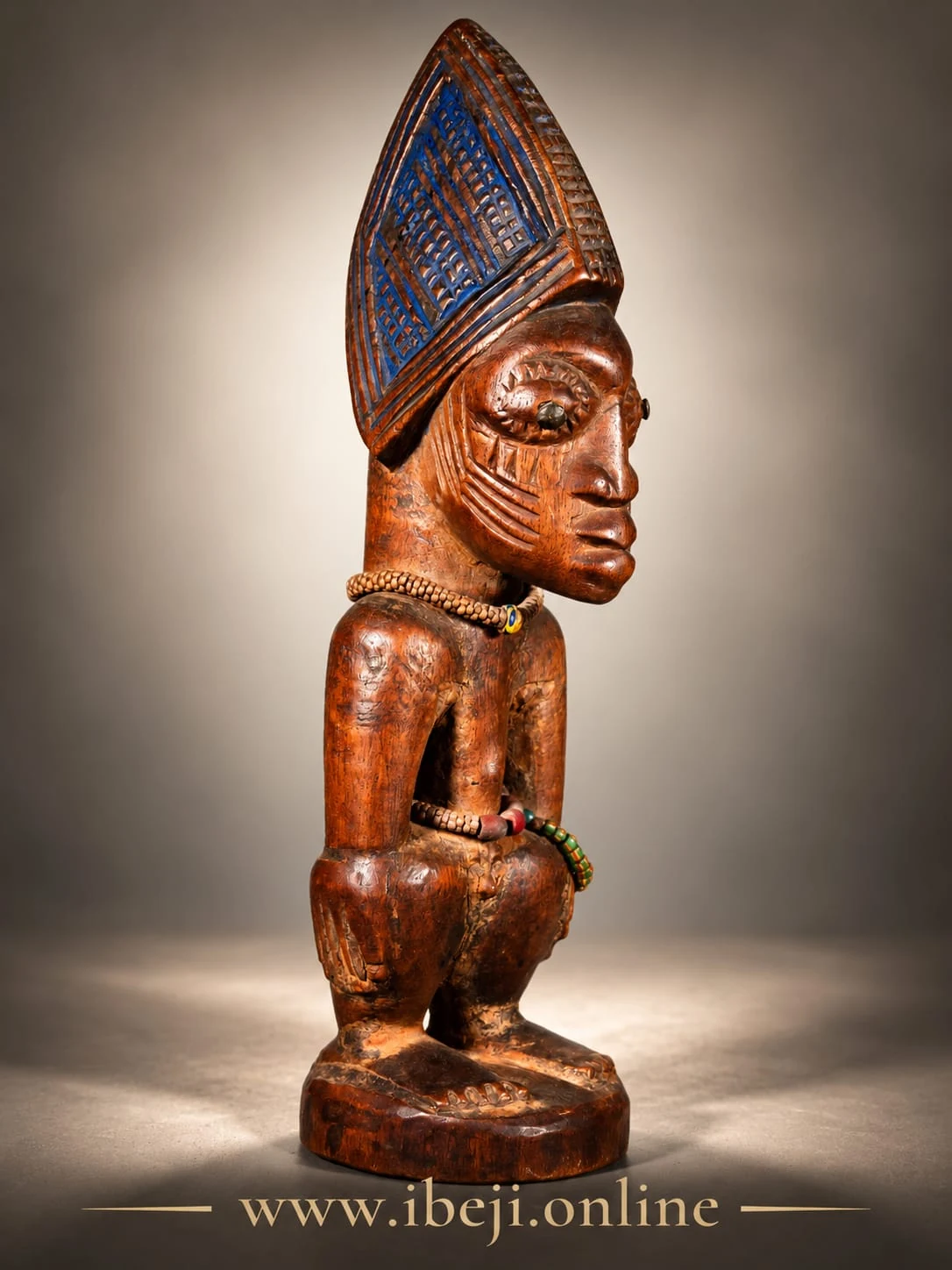 Figura Ibeji vista de perfil, con cofia elevada de tono azul y marcas faciales