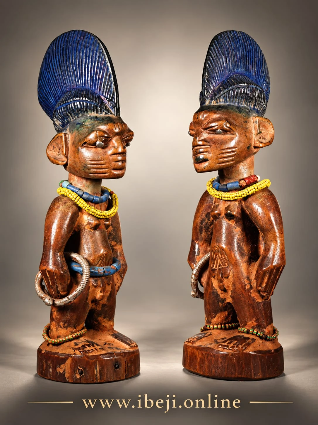 Dos figuras Ibeji con cofias azules y collares, vistas en tres cuartos