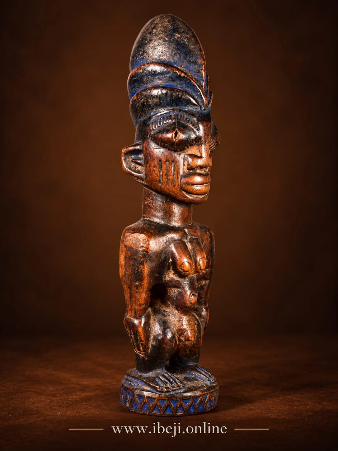 Figura Ibeji de madera con cofia de tono azul oscuro, marcas faciales y cuentas azules en la base