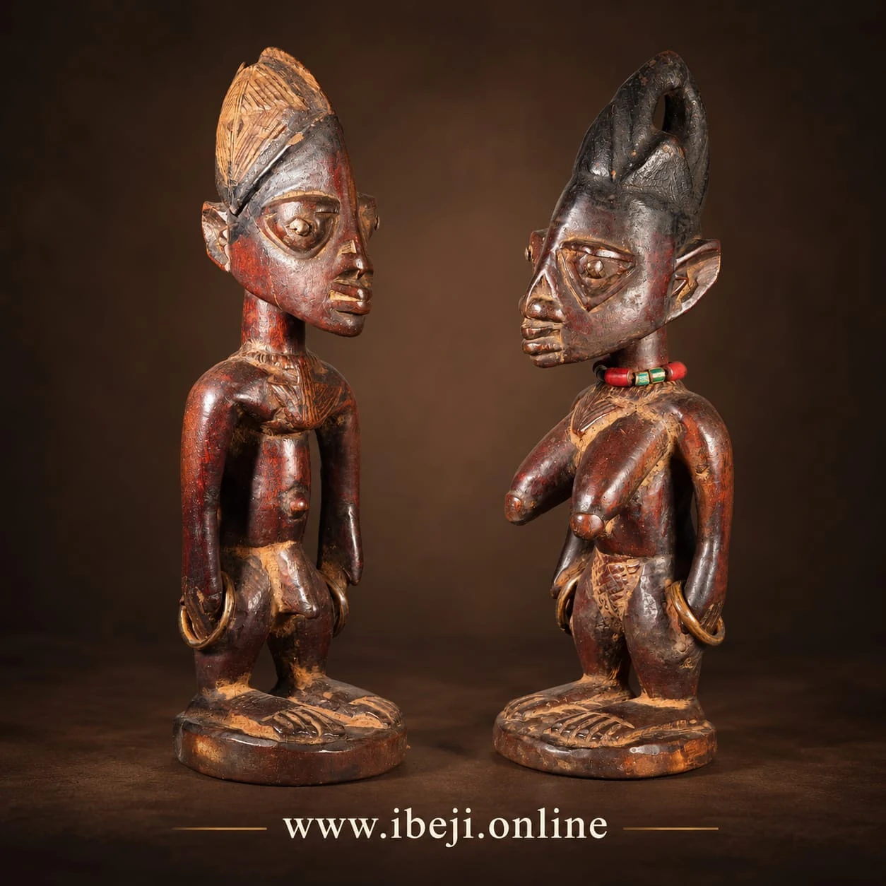 Dos figuras Ibeji de madera vistas en tres cuartos, con cofias distintas y collares de cuentas