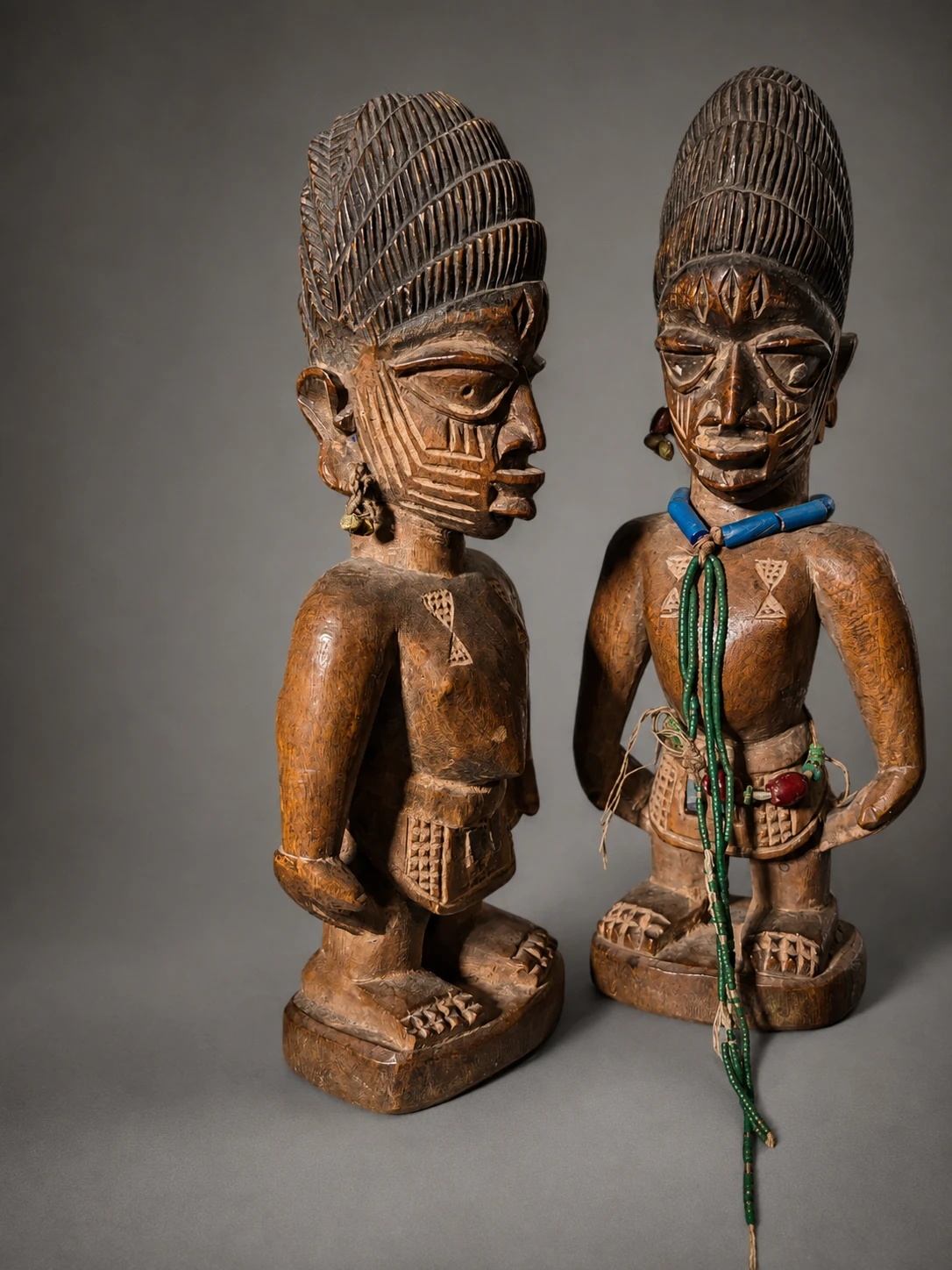 Pareja de figuras Ibeji yoruba con cofias talladas y cuentas de colores