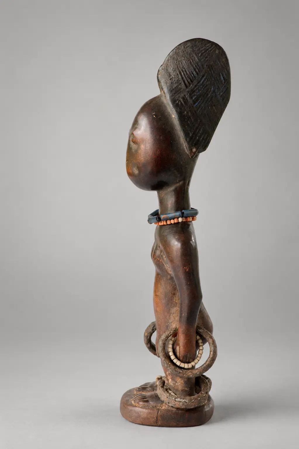 Perfil de una figura Ibeji de madera con peinado elevado, collar y brazalete